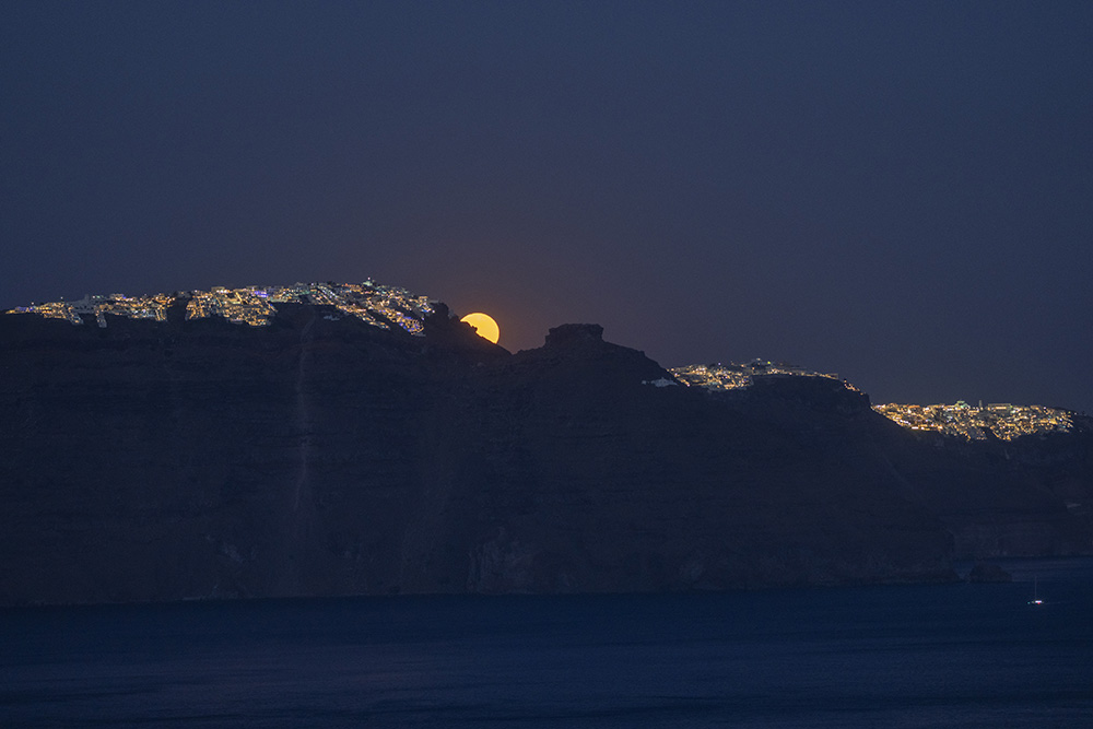 The moon rises behind the village of Imerovigli, left, and the rocky promontory of Skaros, right, on the Greek island of Santorini June 14. (AP/Petros Giannakouris)