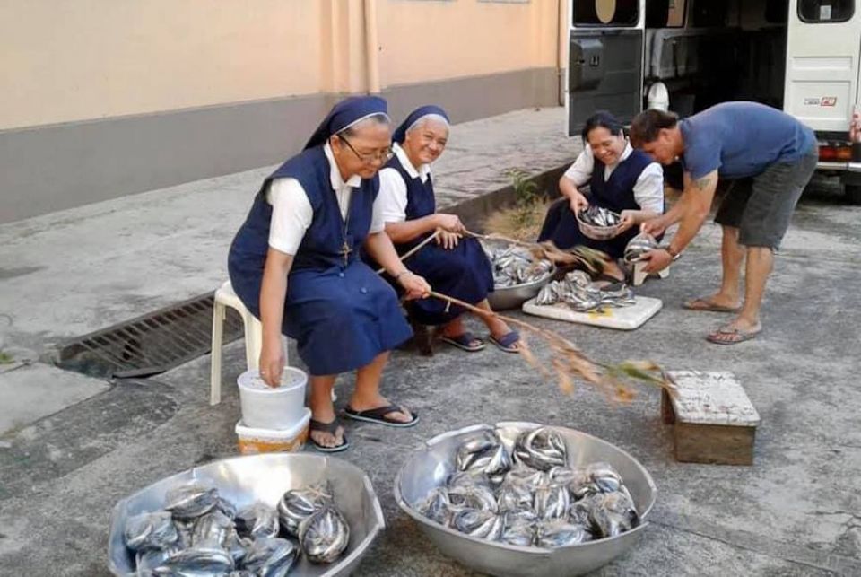 Catholic sisters sitting in chairs in the street with baskets of fish to give away