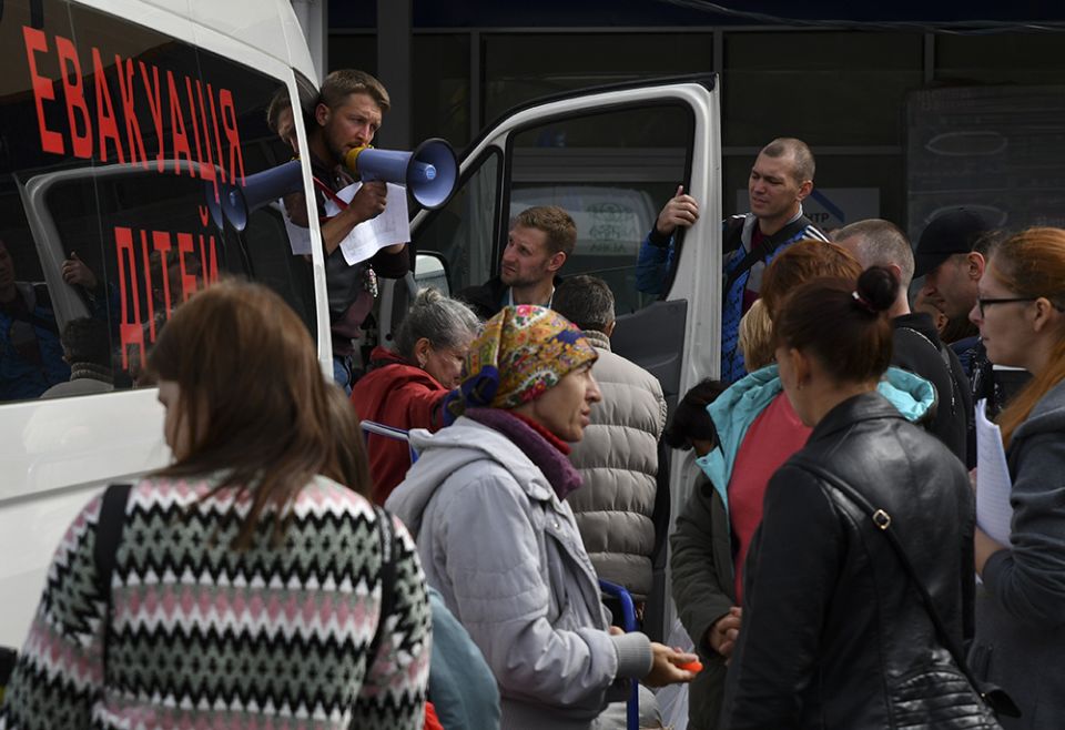 Refugees from war-hit eastern Ukraine stand in line waiting for departure in a refugee center Sept. 15 in Zaporizhzhia, Ukraine. Writing on a bus reads; "Children Evacuation." (AP photo/Andriy Andriyenko)