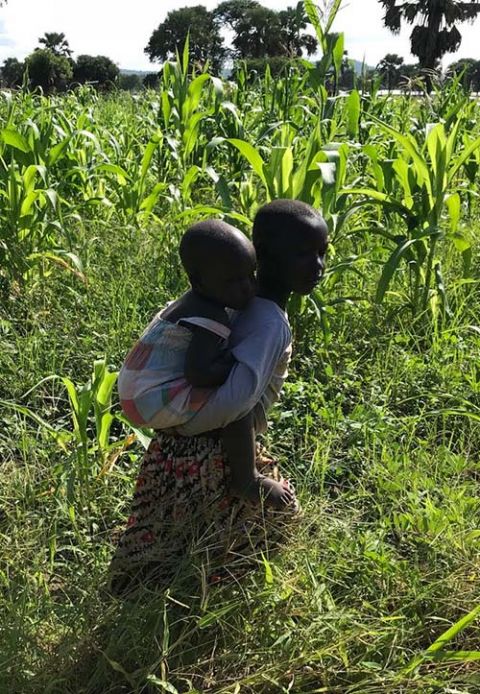 A little girl, Hanna, carries her younger sister to a community celebration in the refugee settlement in Paloyinya, Uganda. (Tere Merandi)