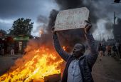 A supporter of presidential candidate Raila Odinga holds a placard referring to electoral commission chairman Wafula Chebukati, while shouting "No Raila, no peace", next to a roadblock of burning tires Aug. 15 in Nairobi, Kenya. (AP photo/Ben Curtis)